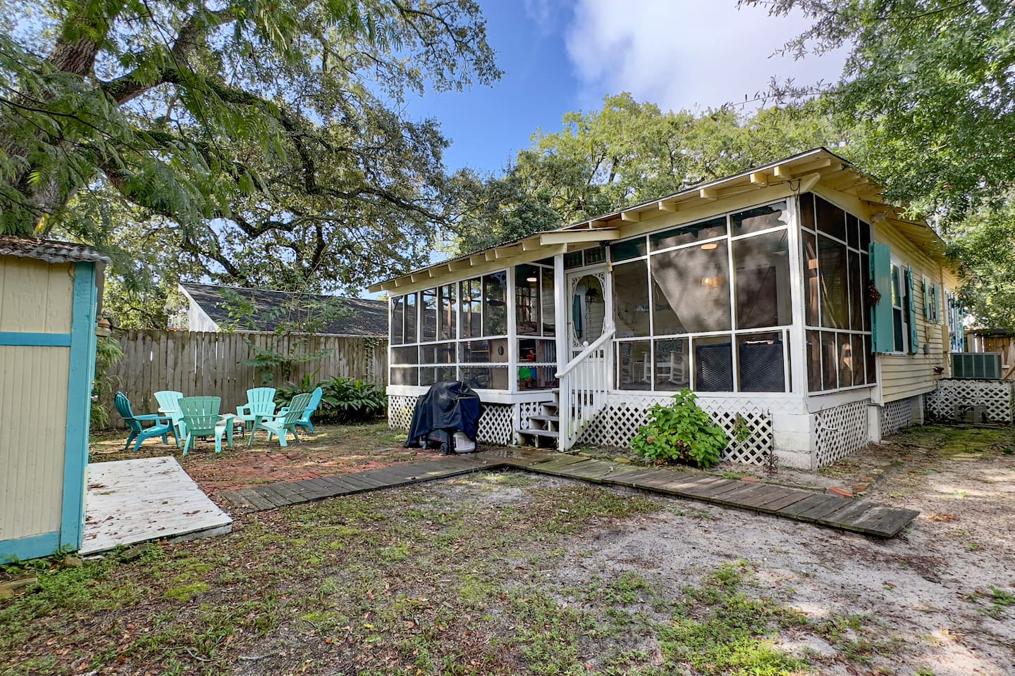 Cozy coastal cottage with a screened porch, shaded yard, and outdoor seating—perfect for relaxing under the trees.