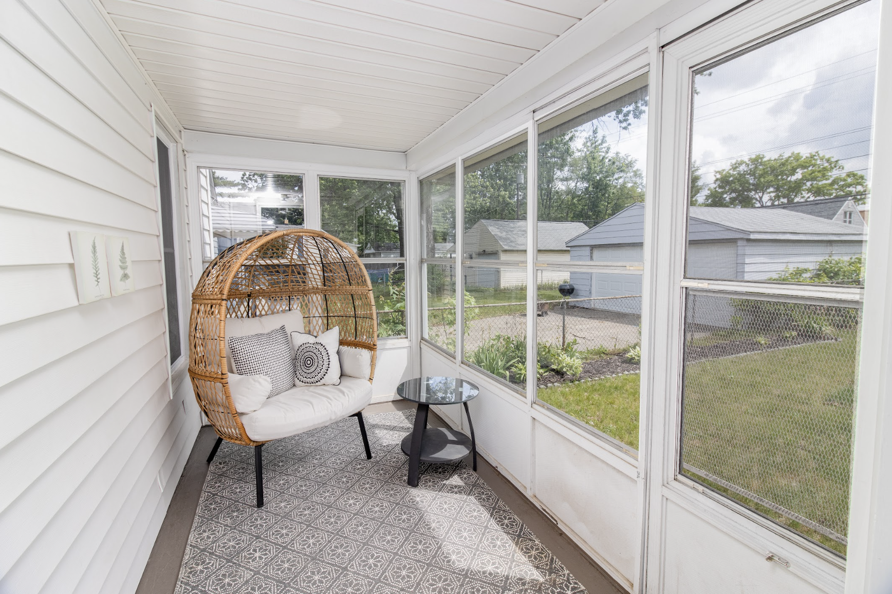 Relax in this cozy enclosed porch featuring a stylish egg chair, charming tile flooring, and peaceful backyard views.