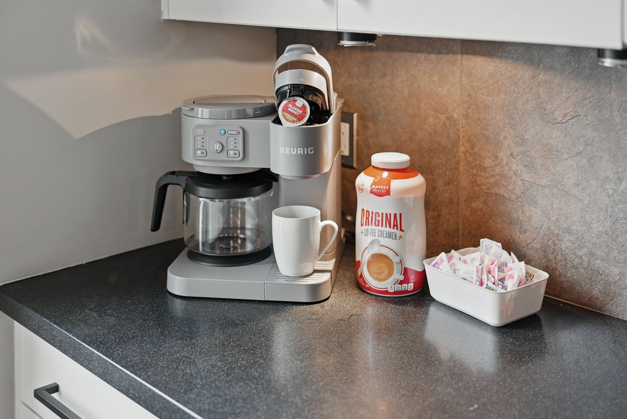 Start your day right with a Keurig dual coffee maker, mugs, creamer, and sweetener—all ready to go at your personal coffee station.
