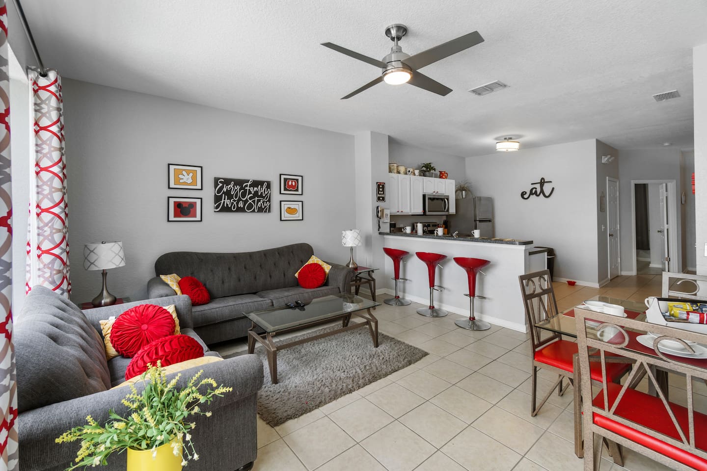 - Open living area with plush seating, bold red accents, and modern ceiling fan  
- Breakfast bar with red stools connects to a fully equipped kitchen nearby  
- Spacious layout ideal for relaxing, dining, and gathering with loved ones