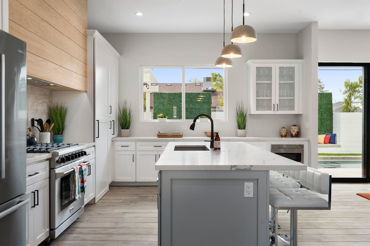 Cook in style with this full kitchen, featuring a spacious island, gas range, wine cooler, and coffee area. White decor with marble, green, and wood accents adds elegance to your culinary experience.