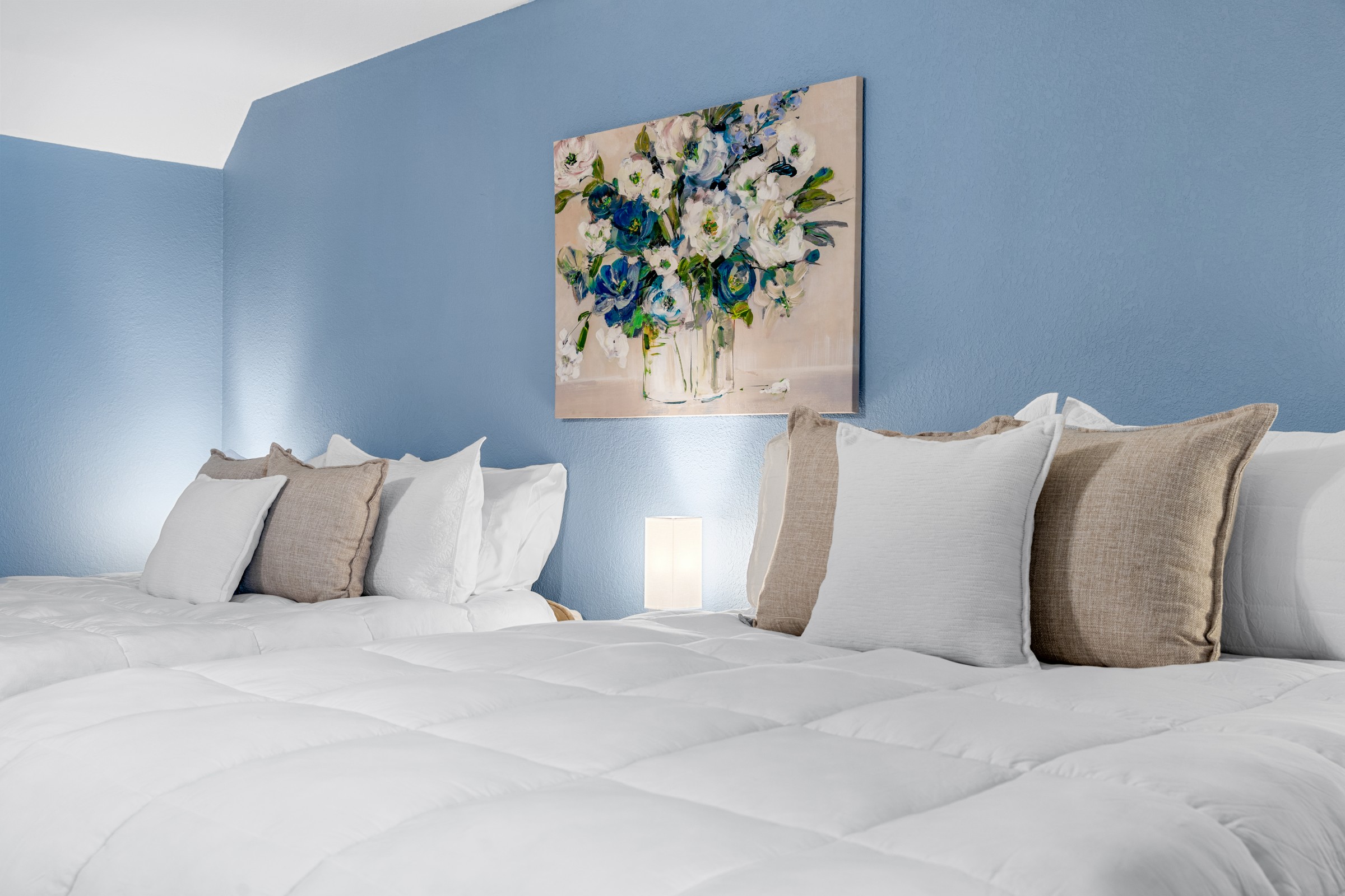 Upstairs bedroom with two queen beds and a blue accent wall. Crisp white linens and floral art make it a calm spot to rest.