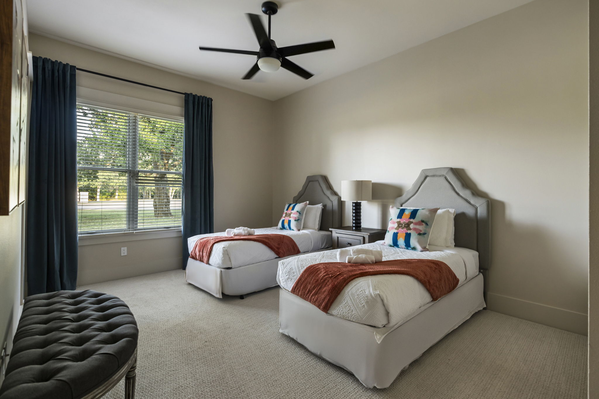 Bright and comfortable with two twin beds, a ceiling fan, and a lamp, making it a cozy space for family or friends.
