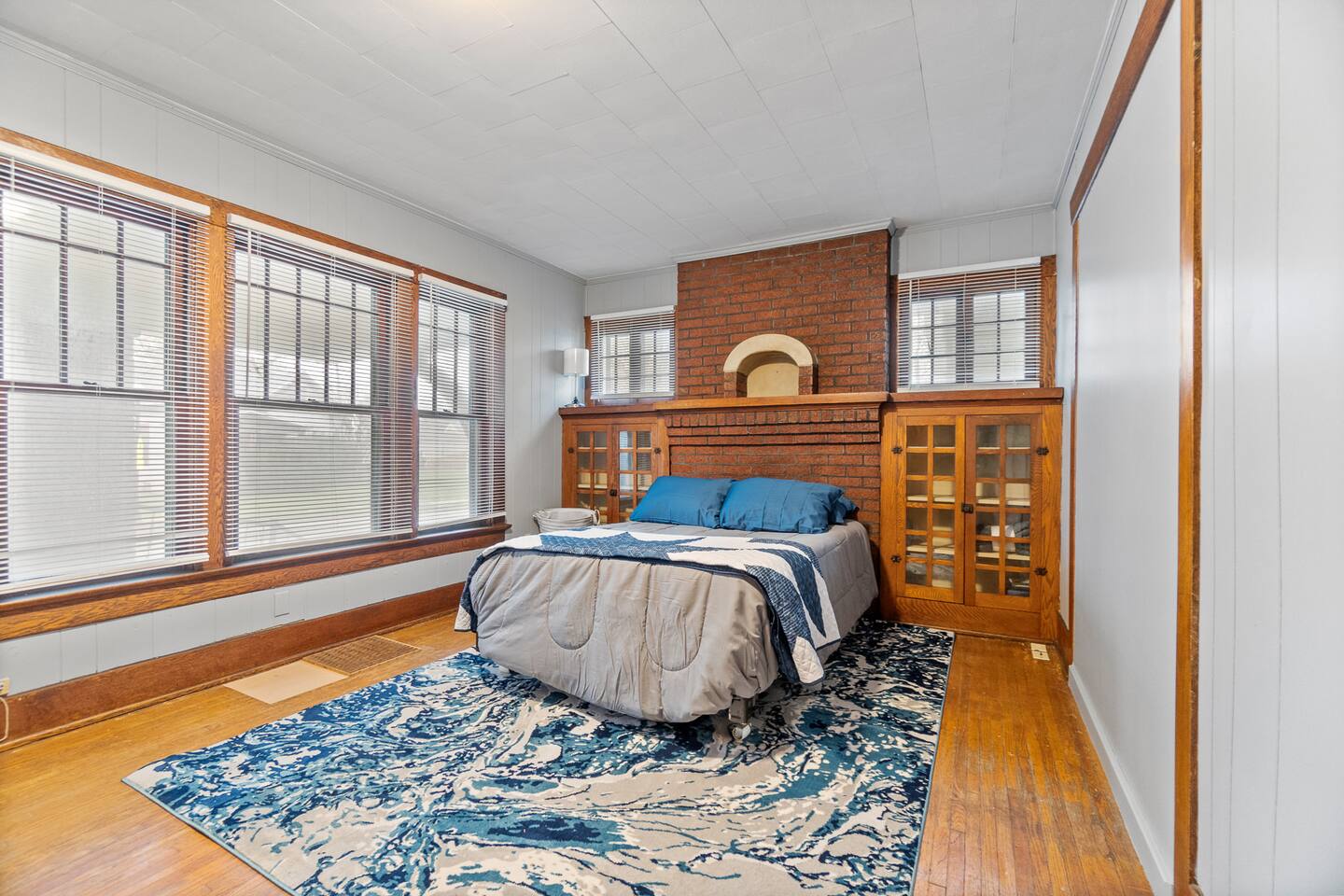 Stylish bedroom featuring a modern sofa with pillows, large windows allowing natural light, a sleek wood cabinet, and a beautifully designed backdrop behind the bed—creating a cozy, sophisticated space with a perfect blend of comfort and style