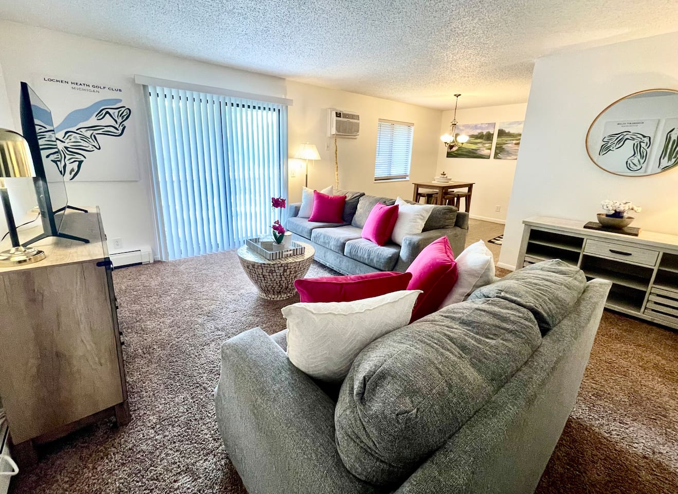 Bright and inviting living area with comfy seating, colorful accent pillows, and natural light pouring in through large sliding doors. Enjoy a cozy night in with the smart TV or gather with friends around the stylish coffee table and open dining space