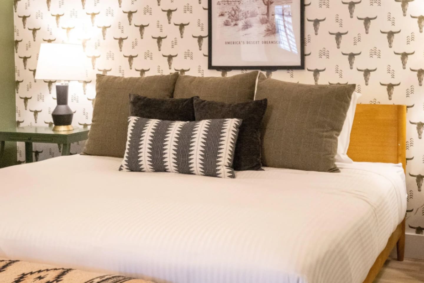 A king bed layered in rich textures, framed by playful ranch-inspired wallpaper — Southwest charm with a boutique-hotel feel.