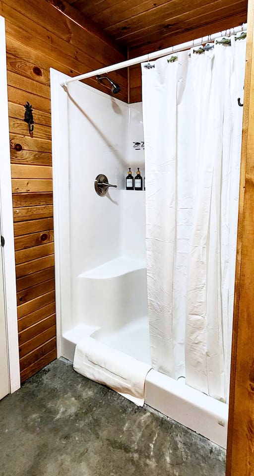Enjoy a refreshing rinse in the clean, step-in shower featuring rustic wood surroundings, a sturdy bench seat, and complimentary shampoo, conditioner, and body wash, everything you need for a cozy, convenient stay.