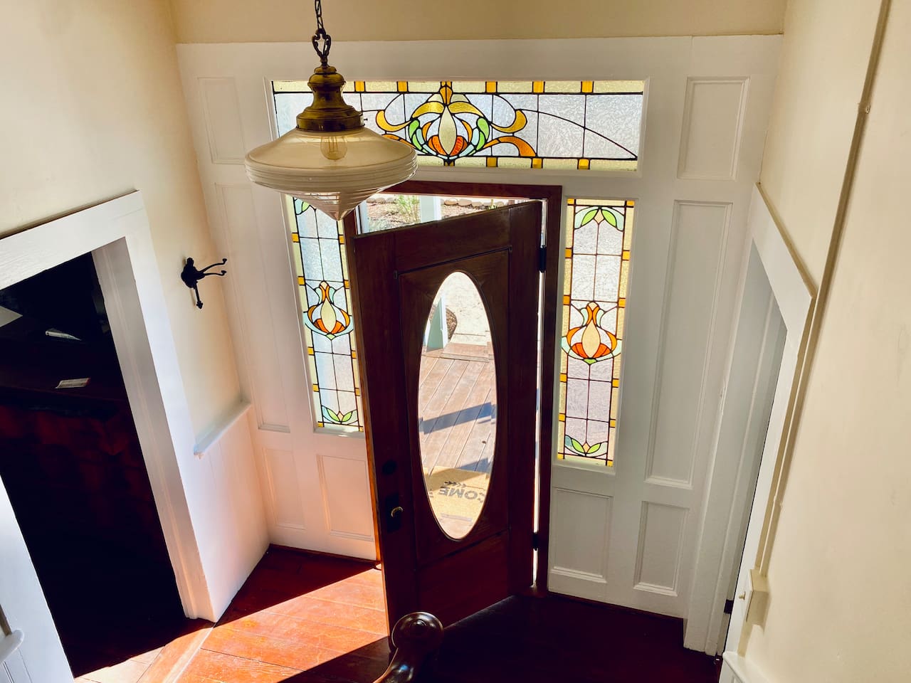 Afternoon light turns the stained-glass entry into a jewel box. The living room opens to the left; the first-floor primary suite—the "Boudoire de Bouge" and private bath—is tucked to the right. Historic charm, thoughtful flow.