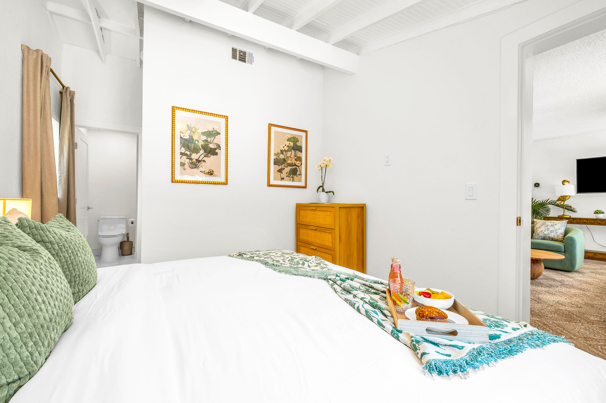 Serene ensuite primary king suite featuring a plush bed with luxury linens, vaulted ceilings with exposed beams, and elegant coastal décor. Includes a spacious walk-in closet with washer and dryer for added convenience and comfort.