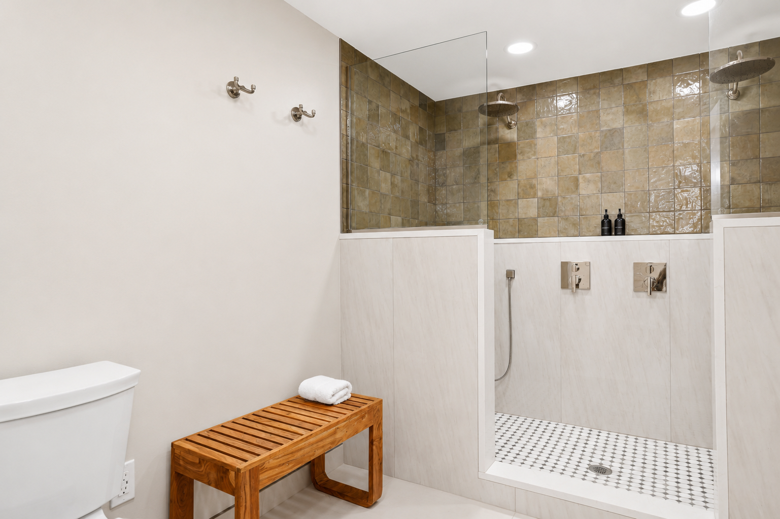 Spa-style walk-in shower with stone tile walls, glass partition, and built-in bench. Clean, modern design with warm tones and a calm, upscale, hotel-like feel.
