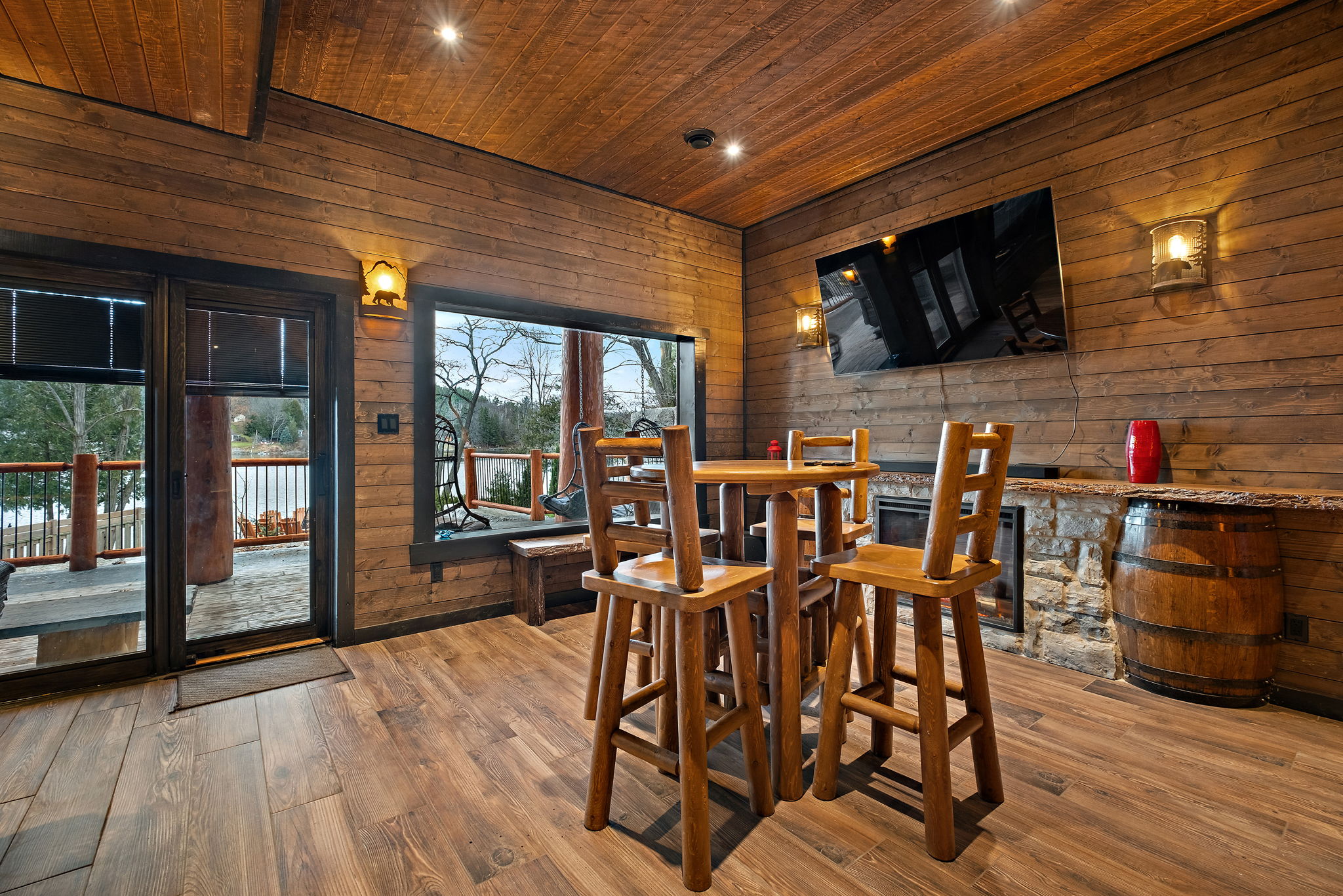 Cozy entertainment lounge with a mounted Smart TV, stone-top bar, barrel accents, and direct access to the outdoor deck.