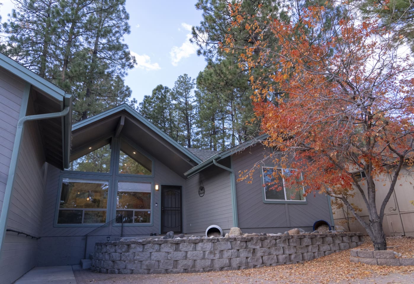 Home entrance with paved courtyard, mature trees, and natural stone details.