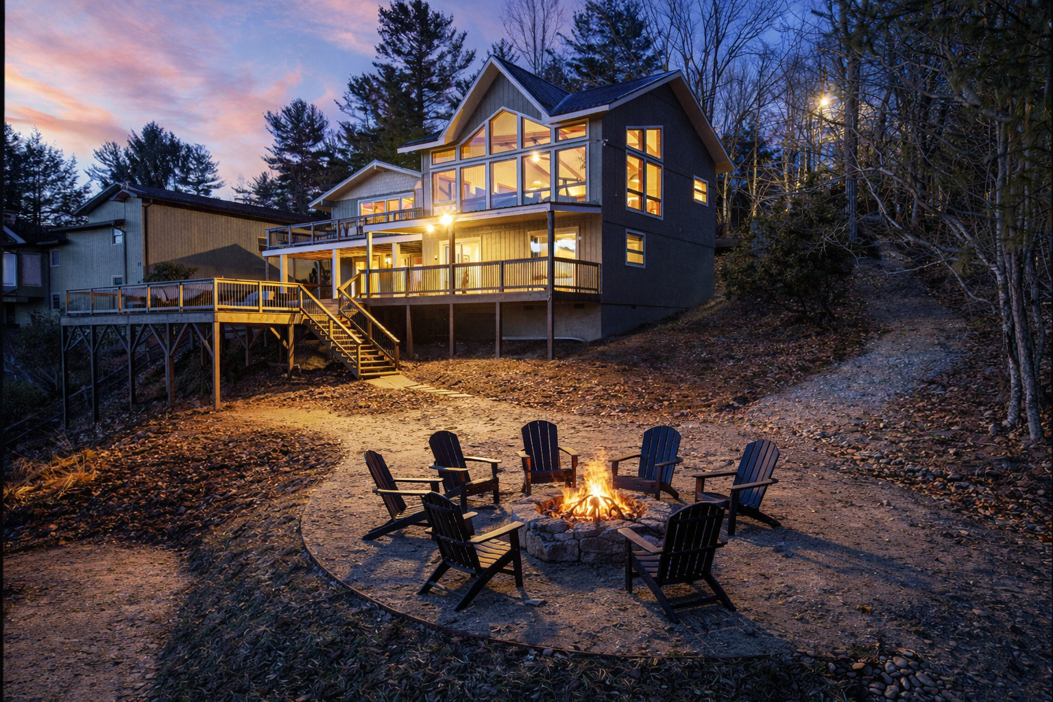 Stone fire pit with Adirondack seating — the perfect spot for evening conversations, s’mores, and stargazing as the house glows at twilight.