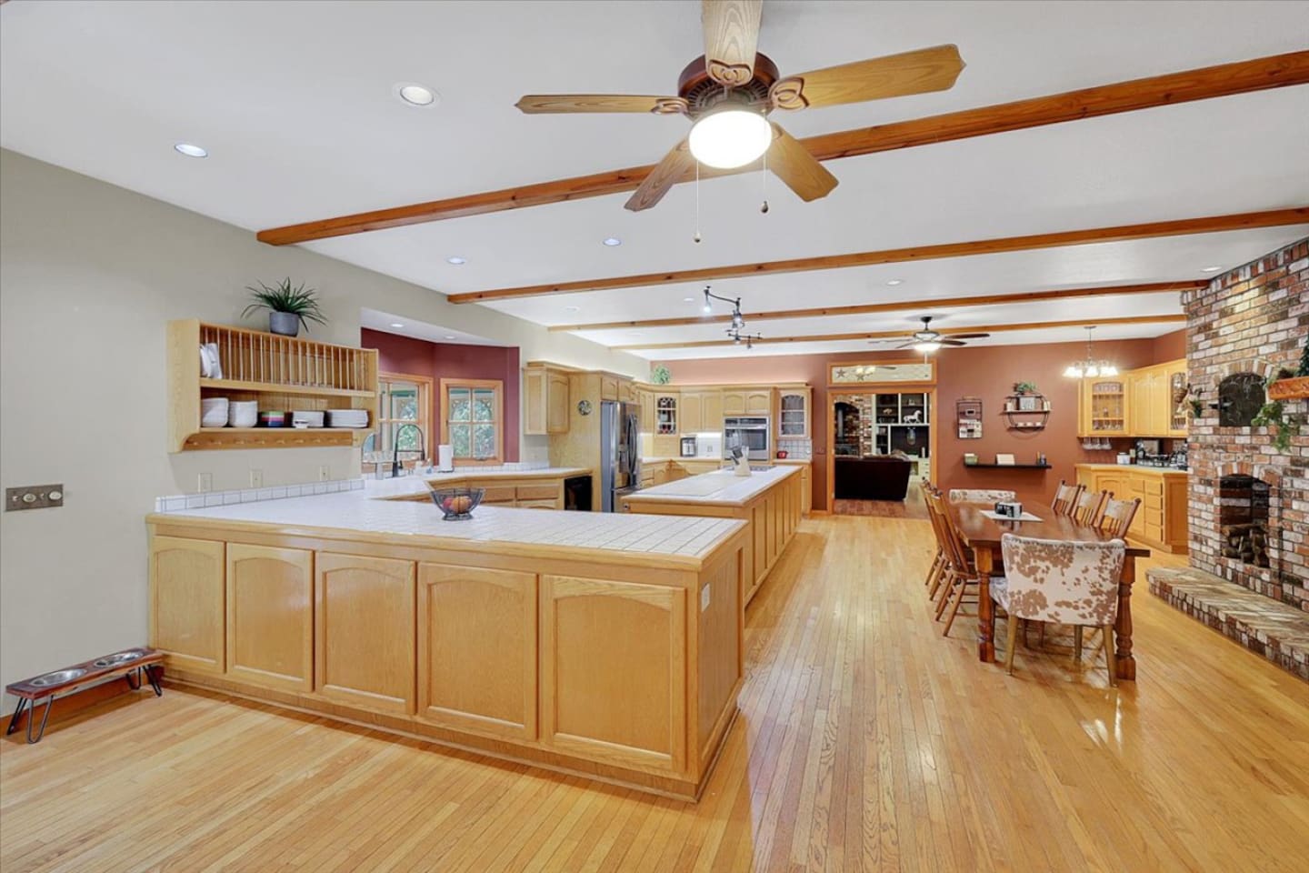 Open kitchen and dining area with lots of counter space, wood floors, and a brick fireplace nearby.
