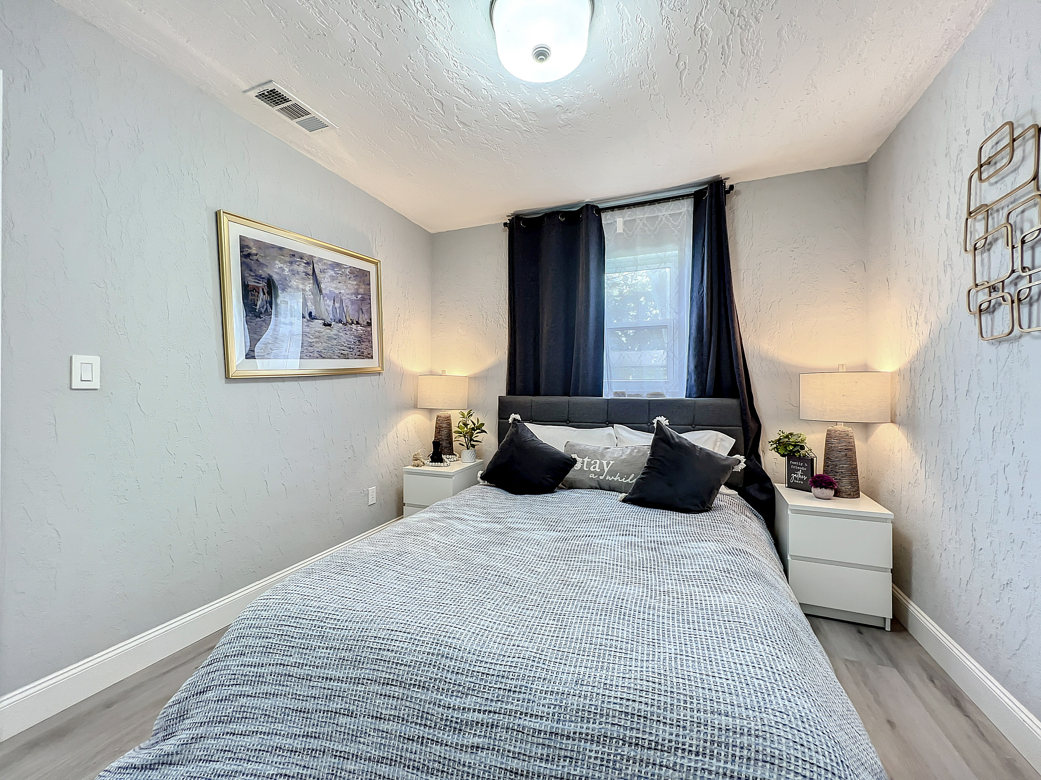 Modern bedroom with queen-size bed, grey bedding, and two bedside tables with lamps.