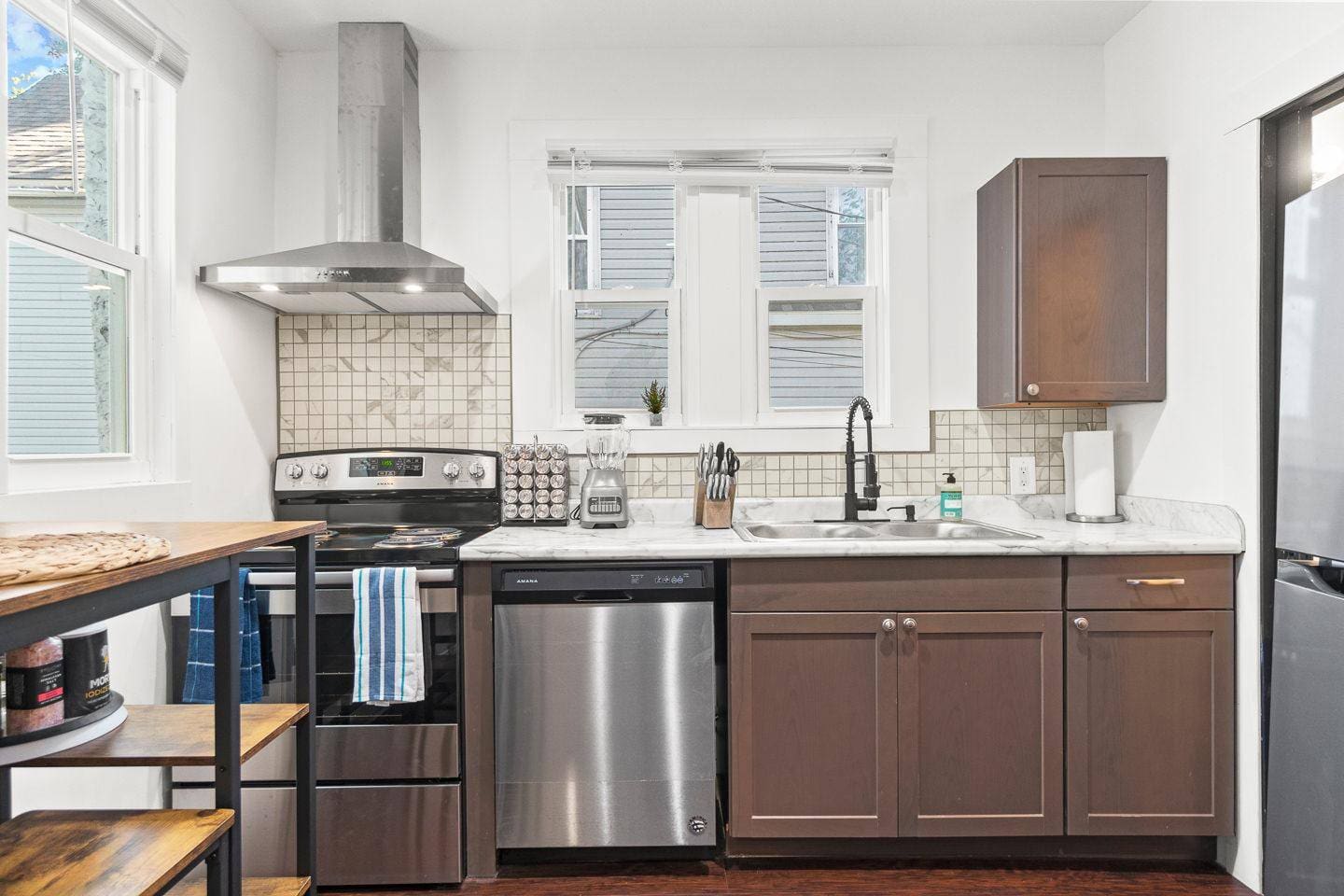 Enjoy cooking in this spacious kitchen, featuring rich brown cabinetry, a full set of modern appliances including an oven, stove, and dishwasher, plus bright windows that let in plenty of natural light. 