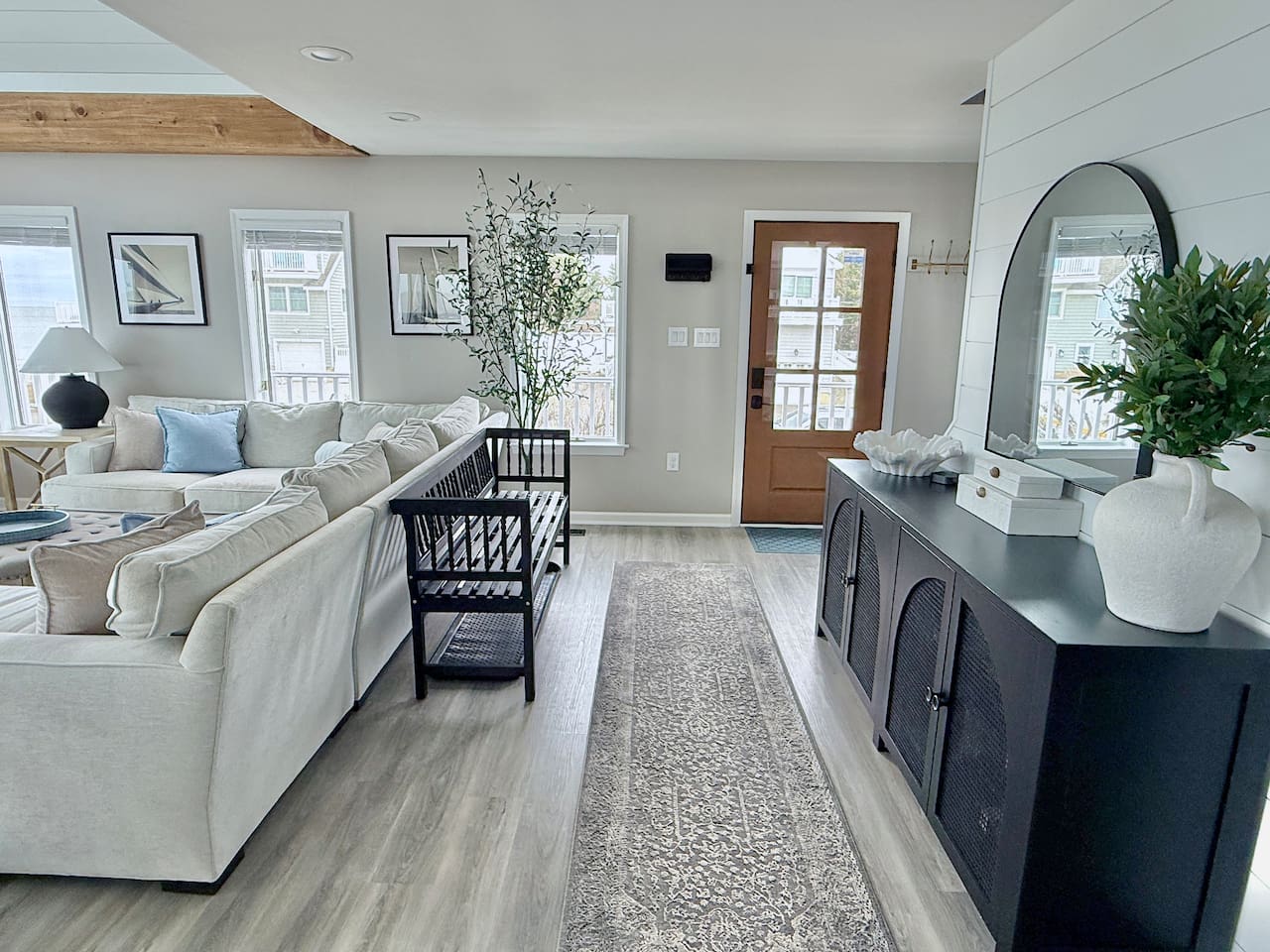 This living area bridges lounge and entry spaces with a large sectional, black accent bench, and cabinet with an arched mirror, perfectly enhancing the home's coastal aesthetic.