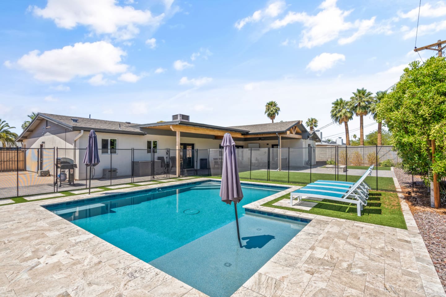 Private backyard pool with safety fence, lounge chairs, umbrella shade, fire pit seating, and a bright outdoor space 