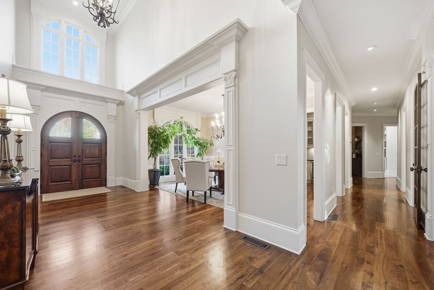 Spacious main dining room to the left of the foyer, featuring a chandelier, seating for seven, and lush green plants. A bright, welcoming space perfect for shared meals or special gatherings.