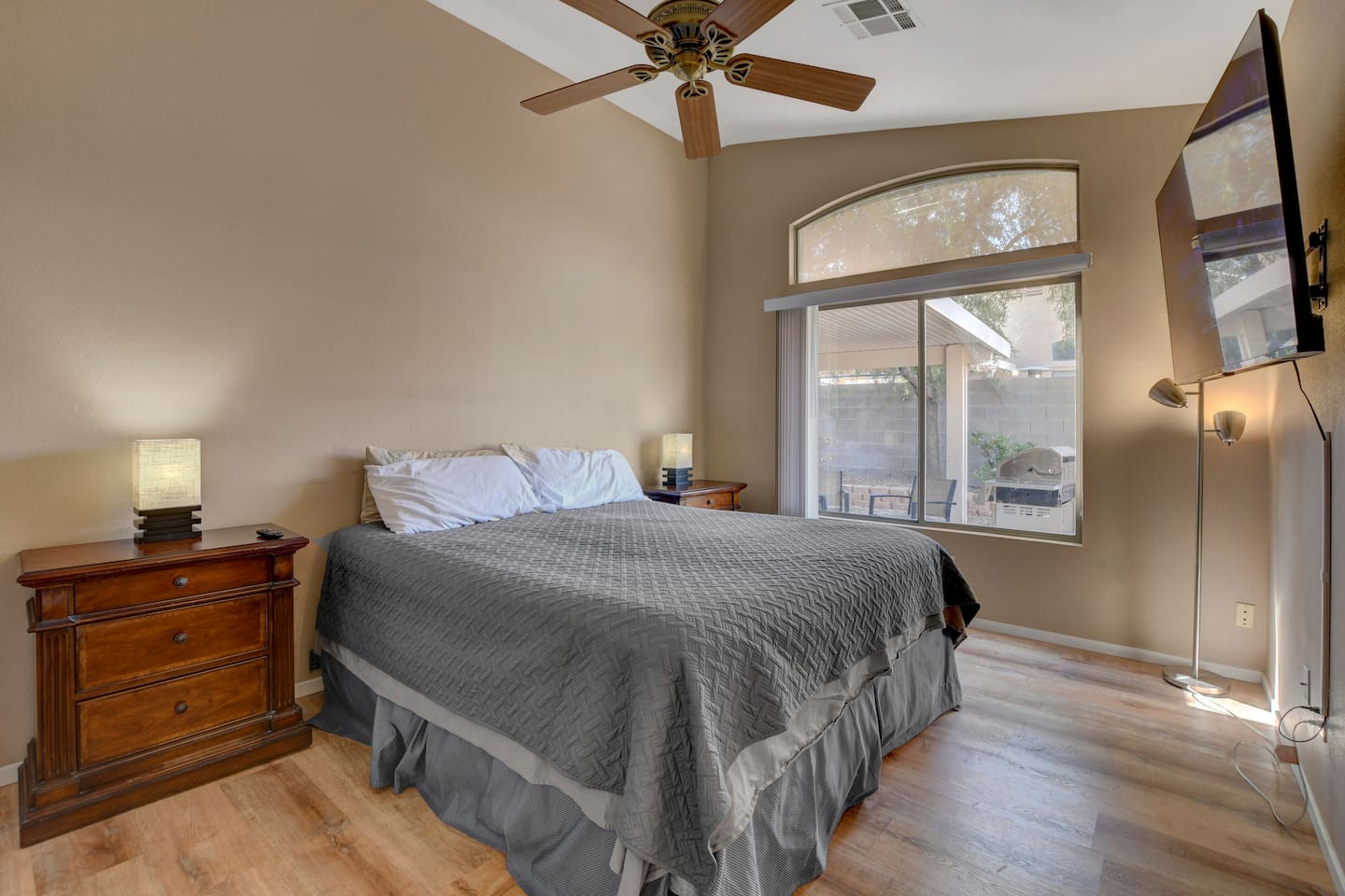 Bright bedroom with TV, ceiling fan, hardwood floors & patio view