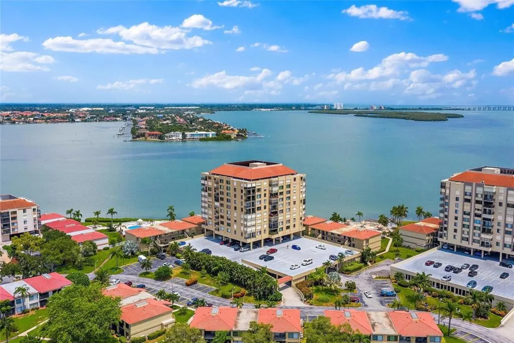 This aerial view showcases the well-maintained, secure building within the Isla del Sol community, surrounded by sparkling bay waters and lush coastal landscaping.