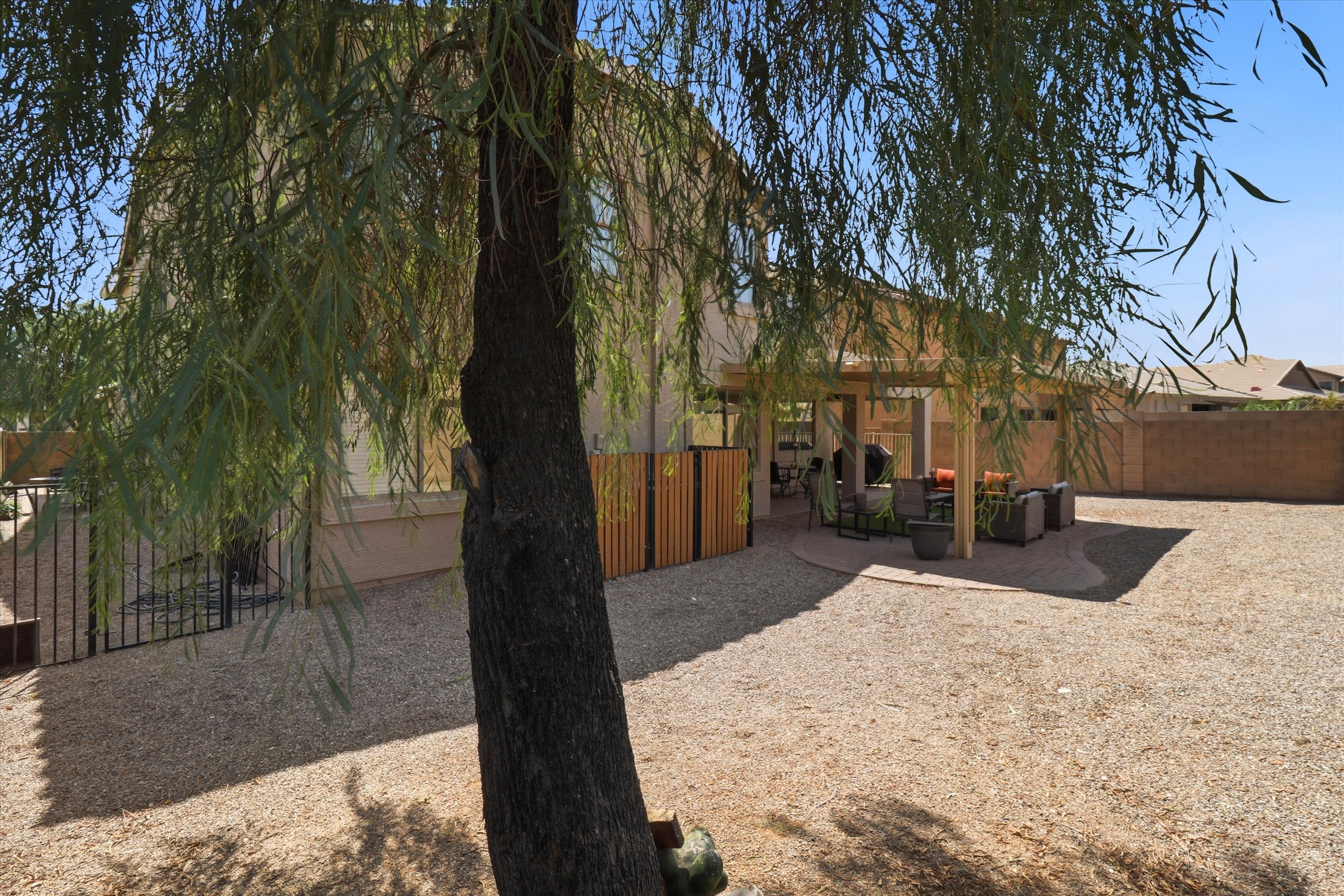 Backyard with a shaded patio, outdoor seating, and a large gravel yard under the trees.
