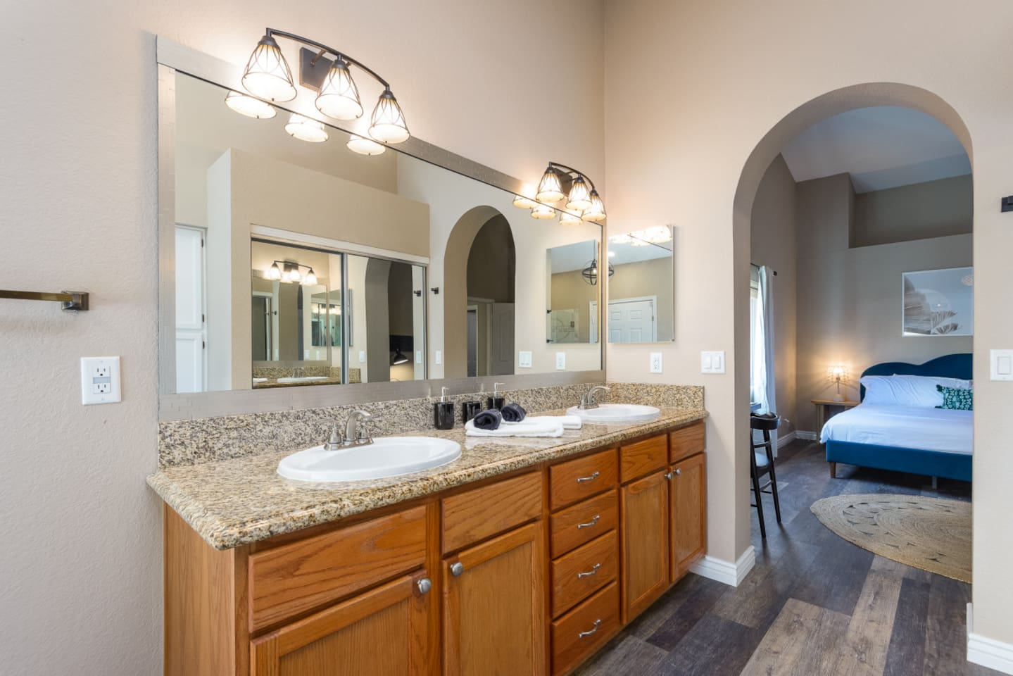 Primary ensuite vanity with double sinks, granite counter space, bright mirror lighting, and direct access from the bedroom.