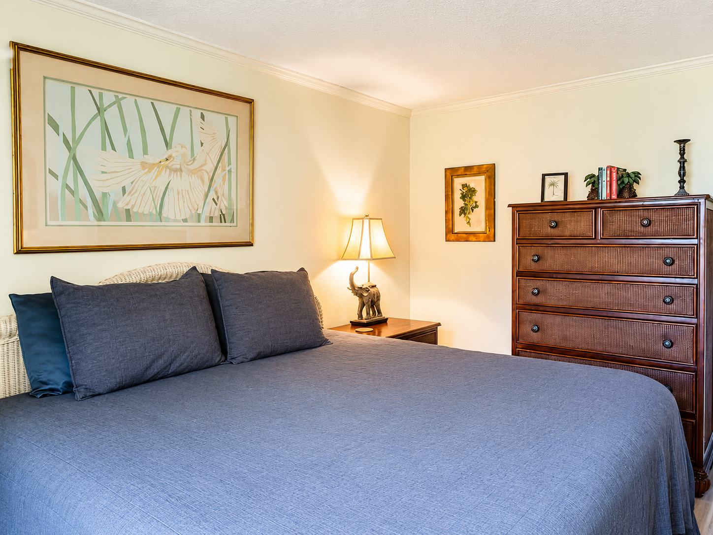 Cozy bedroom with blue‑gray bedding, wooden dresser, and warm decorative accents.