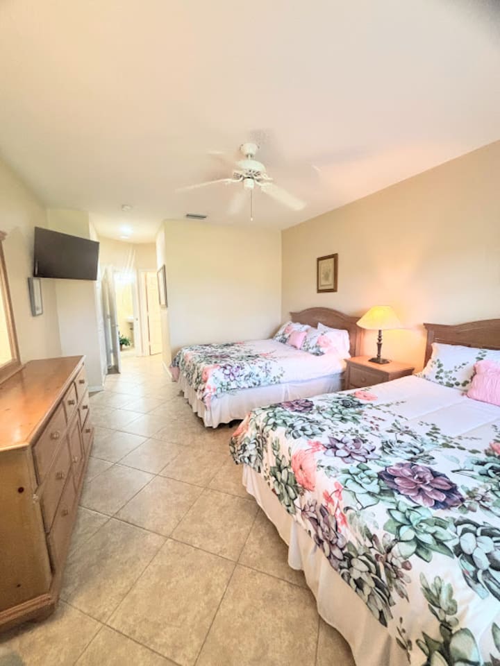 Comfortable bedroom featuring two beds, tile flooring, dresser storage, and a bright, welcoming setup.