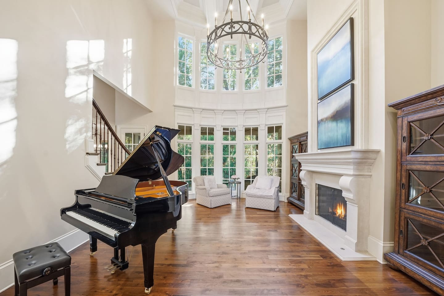 Beautiful entry sitting room with a grand piano, warm fireplace, tall windows, and two comfortable chairs. A bright, serene spot to unwind or enjoy quiet moments.