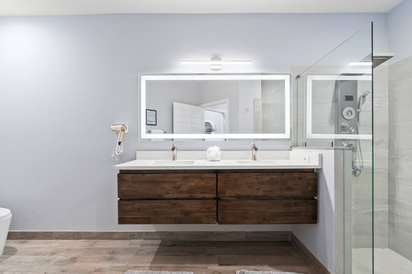 Updated bathroom featuring a wide vanity, modern mirror lighting, wood-look cabinetry, and a glass-enclosed shower.