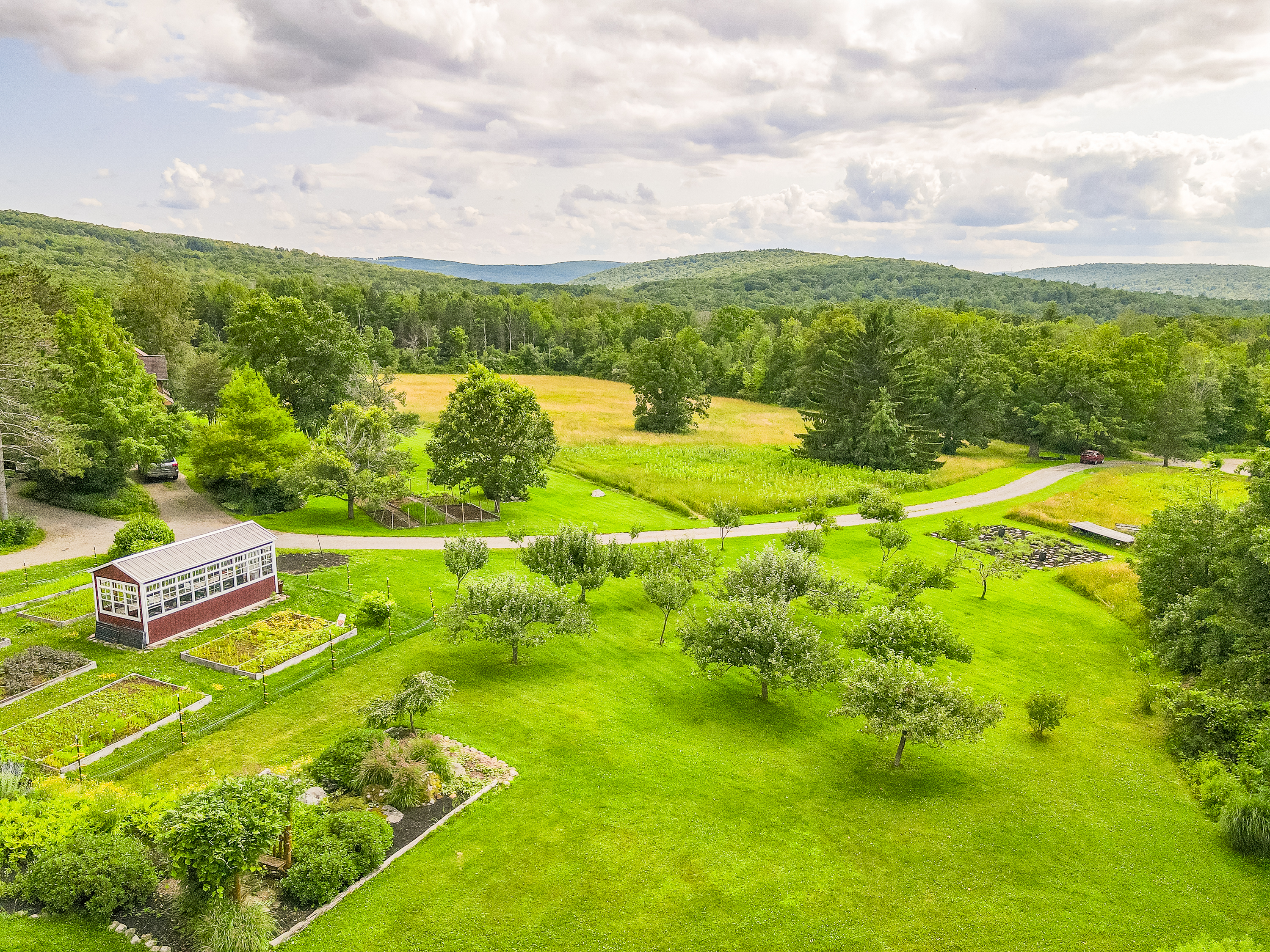 Charming country living with a classic red barn, greenhouse, and lush garden beds surrounded by nature’s beauty.