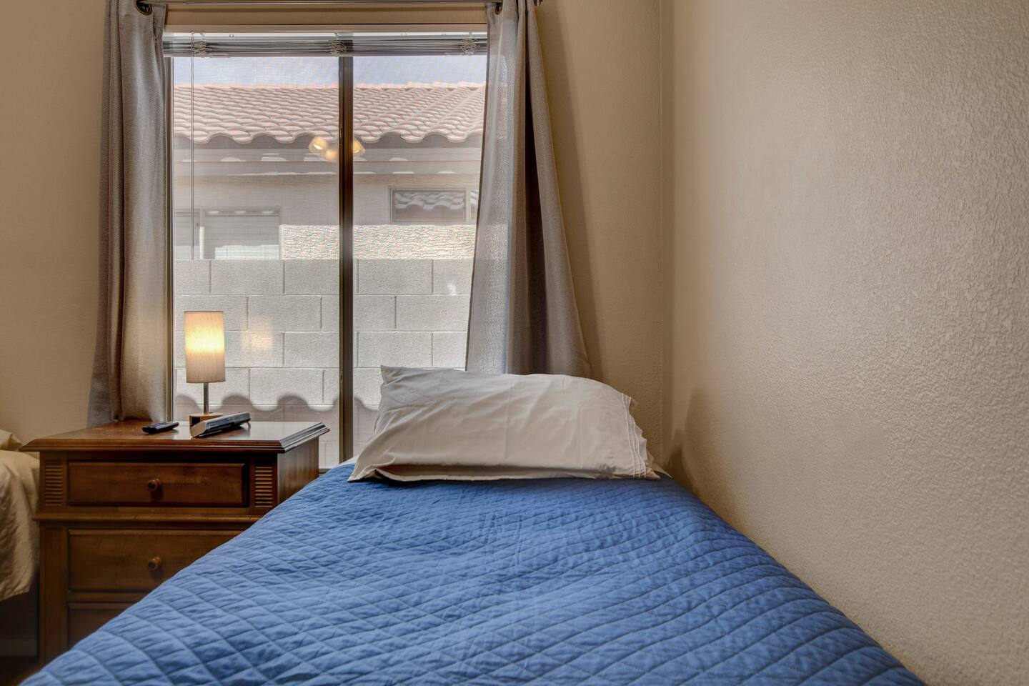 Cozy twin bedroom with window light, lamp, and bedside storage.
