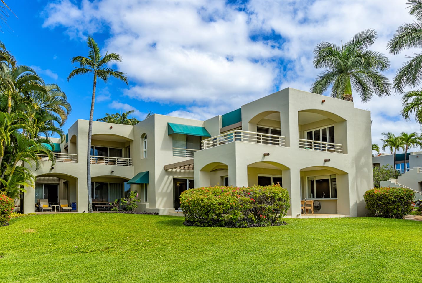 Your ground-floor condo is partially concealed behind the bougainvillea hedge. The turquoise awning center-left is your bedroom window, the wrap-around lanai to the right of the awning. This is a four-plex.