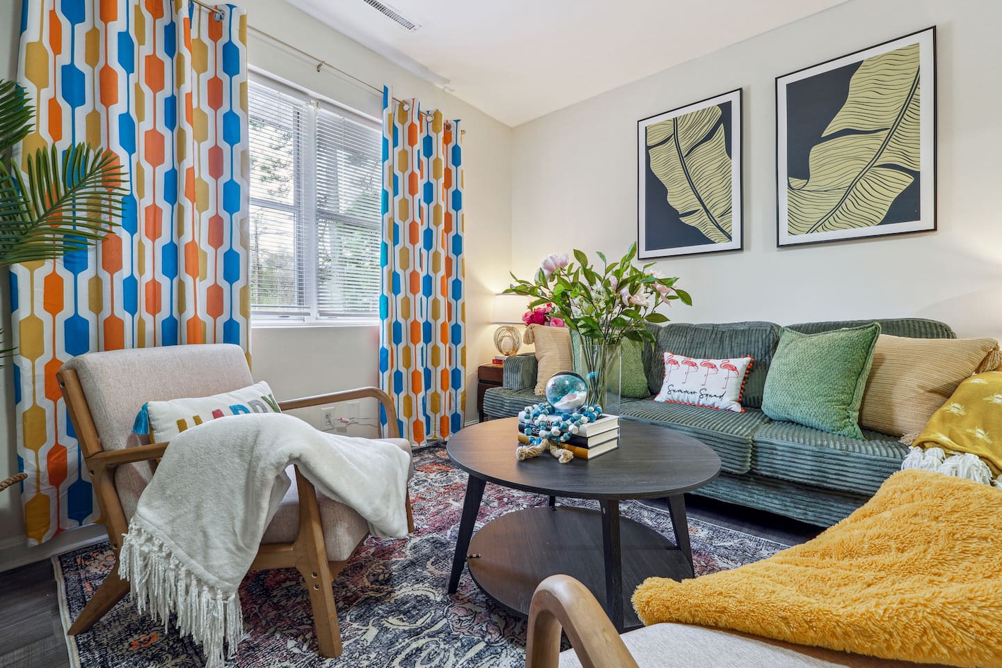 Enjoy a cozy living room featuring a long comfortable sofa, a TV for your entertainment, a ceiling fan, two chair, and a window with a lovely view outside — perfect for relaxing and unwinding.
