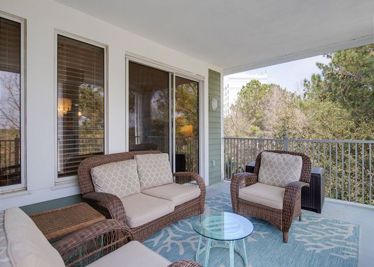 Covered balcony with wicker loveseat and armchairs, outdoor rug and glass side table