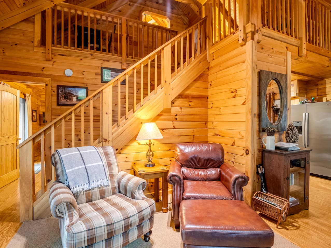 Cozy living room seating area with comfortable chairs, warm cabin charm, and staircase access to the loft