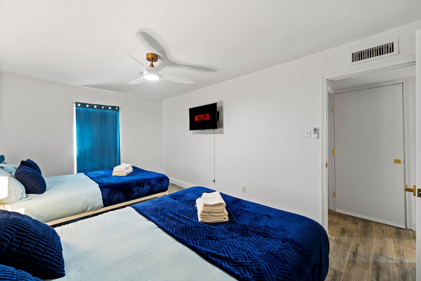 Spacious bedroom with two plush queen beds, blackout curtains, and a smart TV—ideal for families or groups to unwind in comfort.