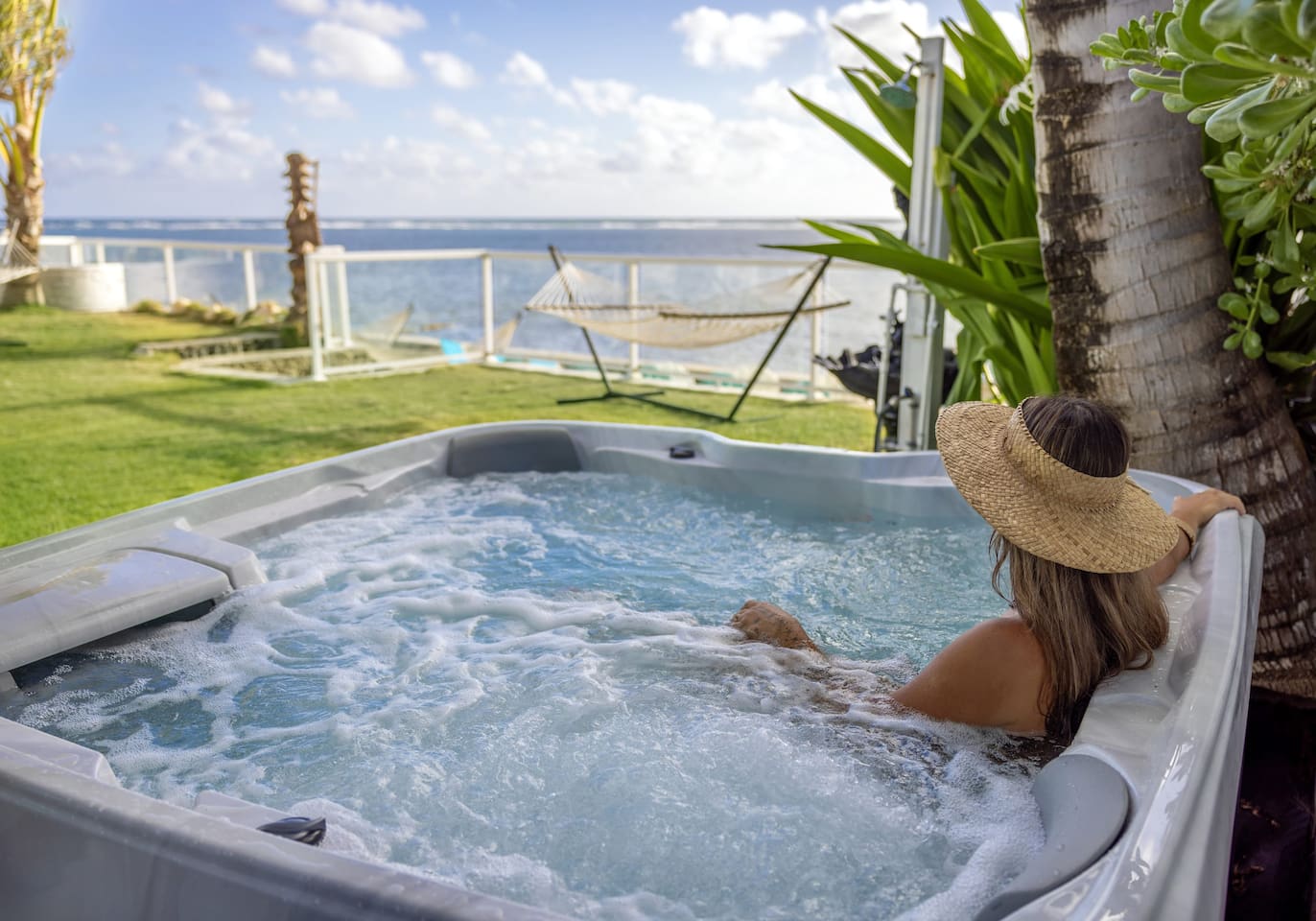 A state-of-the-art latest 7-person Jacuzzi-brand beachfront jacuzzi with full-body length lounger seats, cupholders and cushioned captain's headrests overlooking a crystal clear turquoise blue ocean.