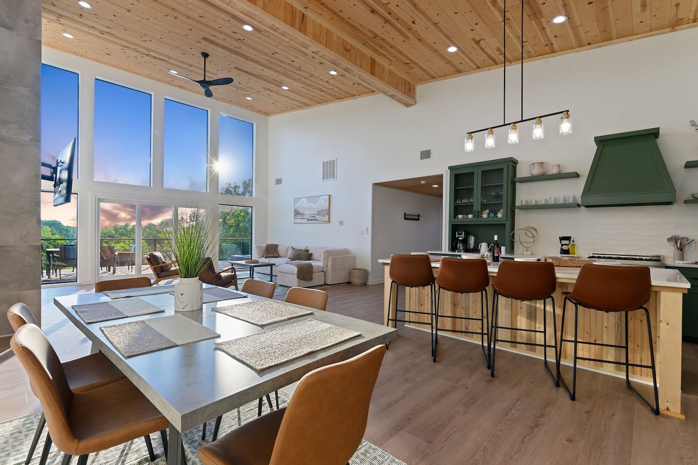 Open-plan dining and kitchen with a large island and floor-to-ceiling windows overlooking the trees.
