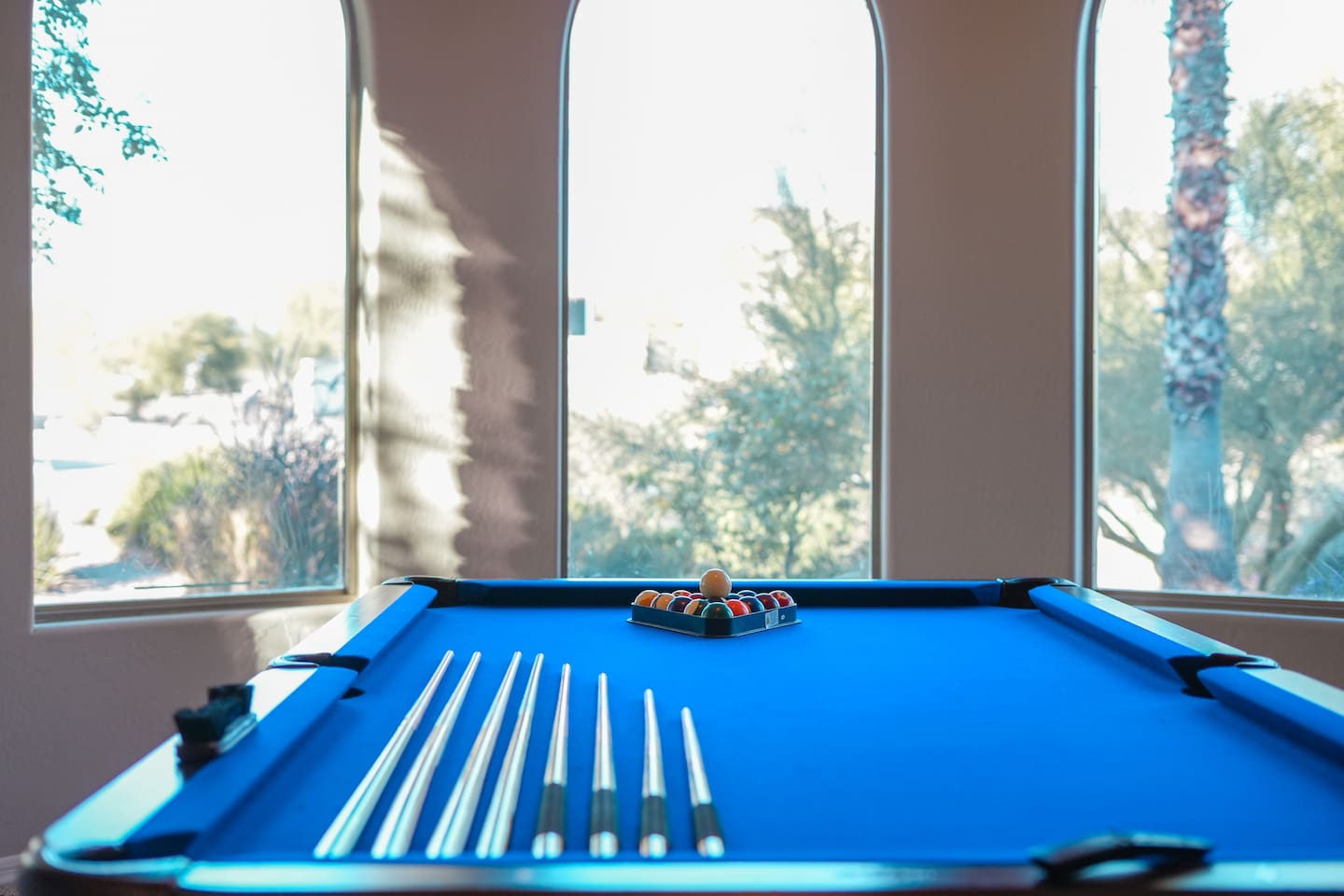 Wide angle highlighting the pool table framed by large windows and serene outdoor views.