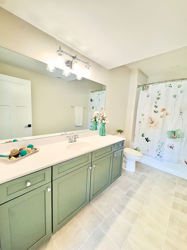 A spacious en-suite master bathroom, mirrors the serene color palette of greens and neutrals of the bedroom to offer a spa like retreat.