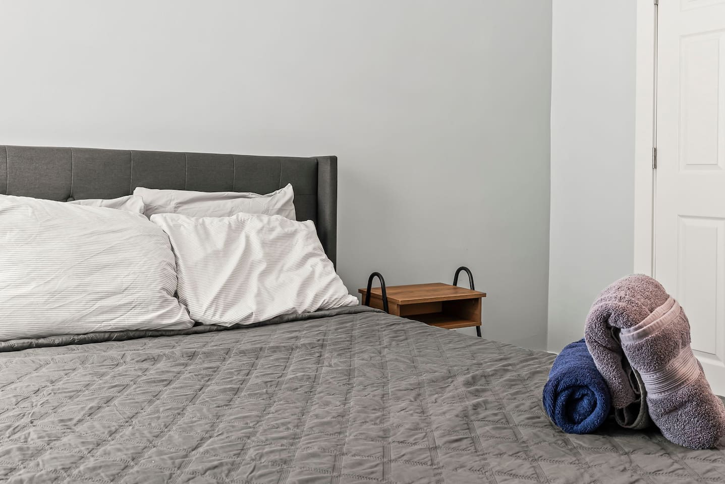 Clean and inviting sleeping area with full-size bed, folded towels, and convenient bedside storage.