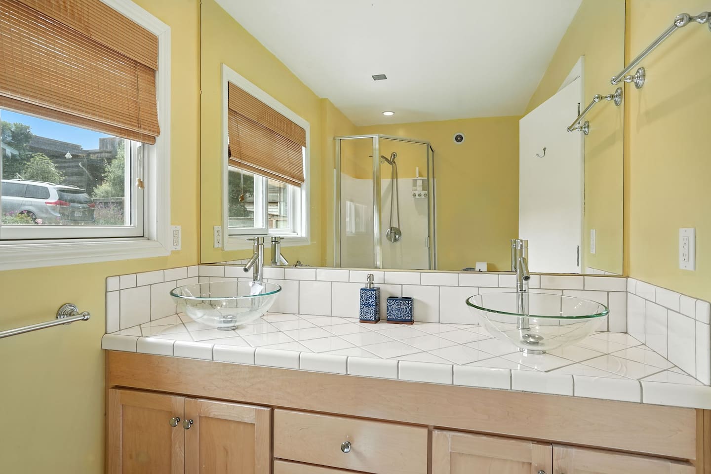 - Bright bathroom with dual glass vessel sinks and large mirror  
- Tiled countertop and natural wood cabinetry create a warm, inviting feel  
- Walk in shower and windows bring in natural light for a fresh start to the day  
