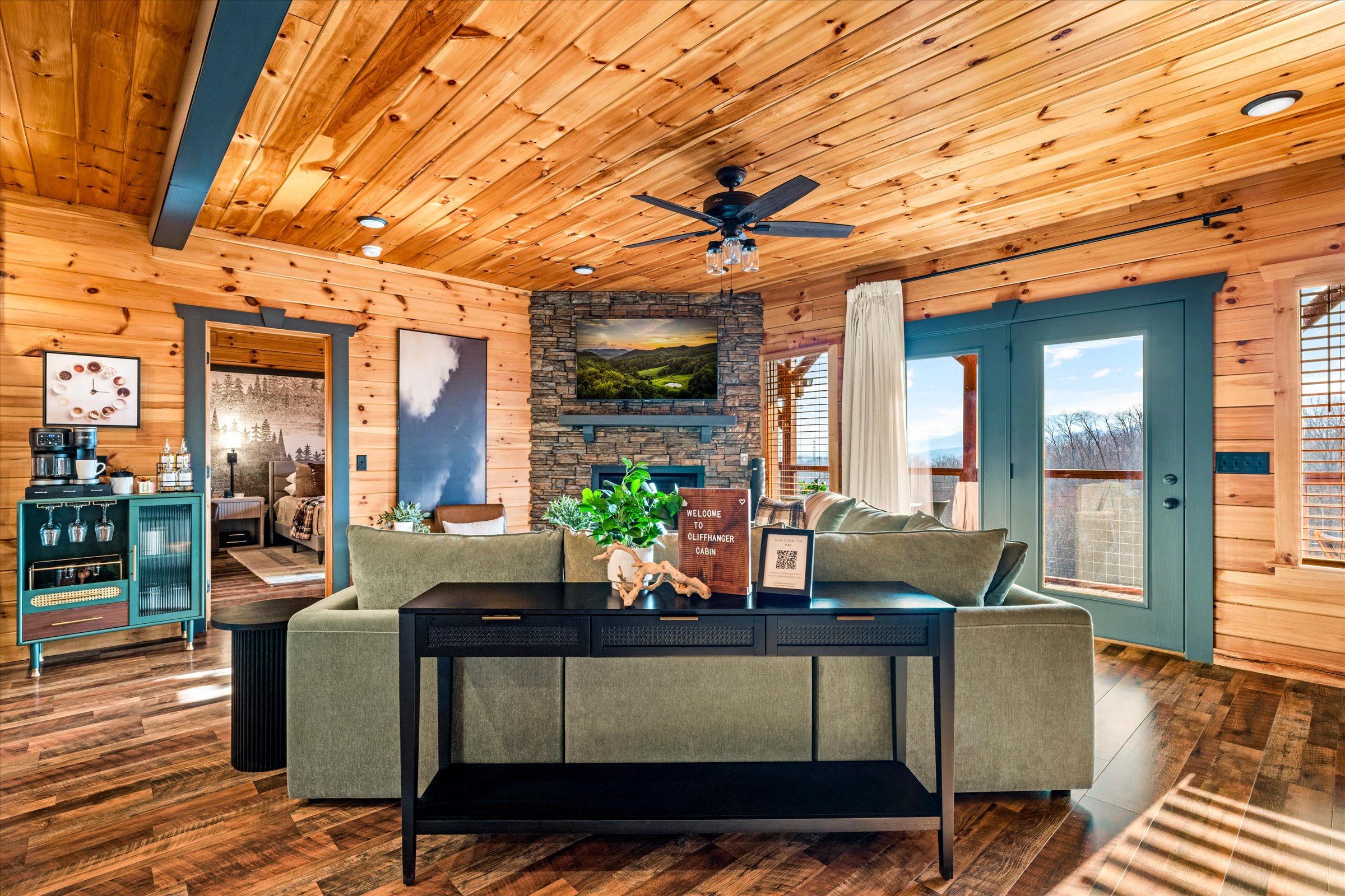 Spacious open-concept living room with cozy seating, stone fireplace, and direct access to the deck with scenic views