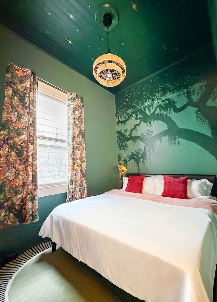 Moody green bedroom featuring a hand-painted Louisiana oak mural and starry night ceiling. A cozy, atmospheric space inspired by the magic of New Orleans. Features a king bed, plush linens, full-size mirror, a live oak mural, a secret speakeasy.