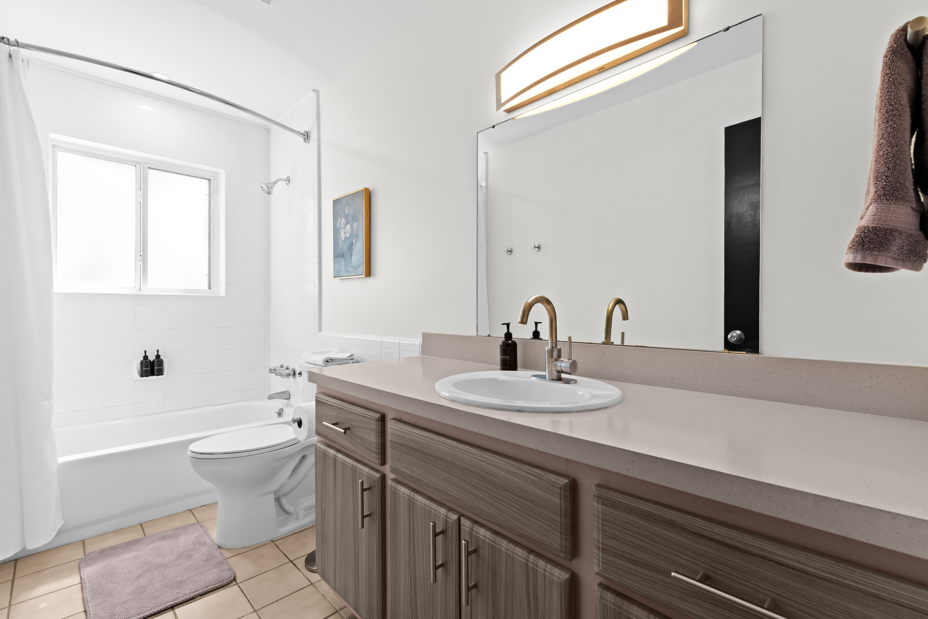 Clean and modern bathroom with vanity, large mirror, and full-size tub/shower.