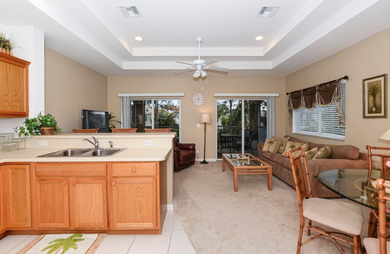 Spacious kitchen and living area with tray ceilings, breakfast bar seating, and sliding glass doors leading to the screened balcony.