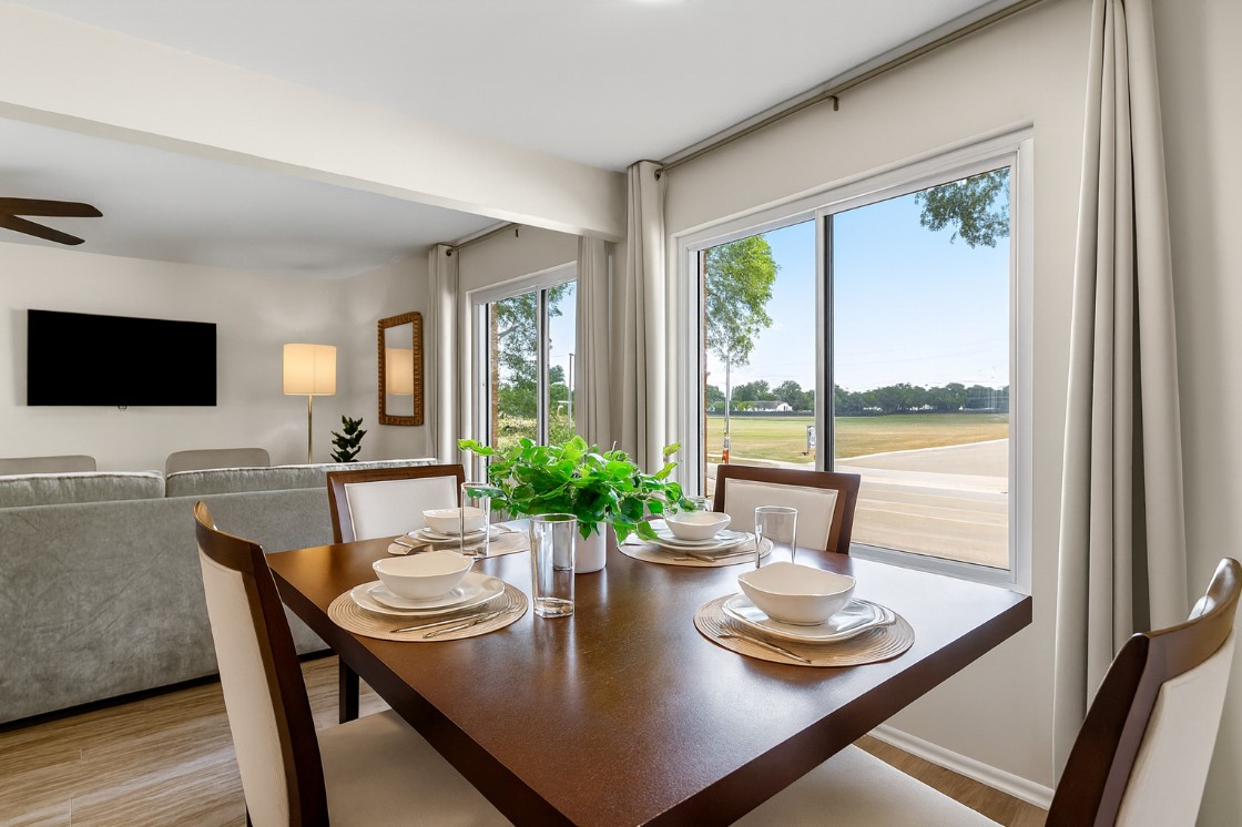 Bright dining area with large windows, natural light, and a stylish table setup overlooking the living room—perfect for meals with a view.
