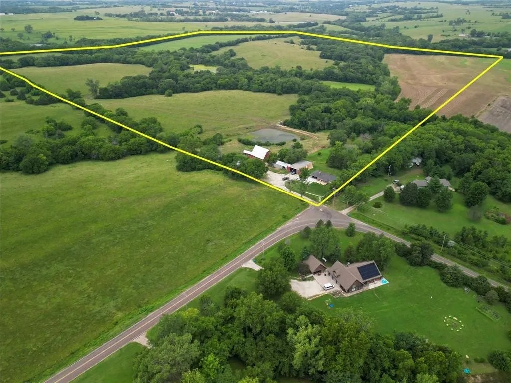 This aerial view shows the full scope of the property, highlighting wide-open fields, wooded areas, and the peaceful setting that surrounds the farmhouse—offering privacy, quiet, and room to relax.